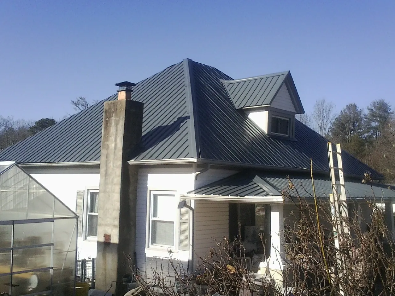 Dark blue standing seam metal roof on a white farmhouse with dormer — Slate & Tile Roof Repair by Roofing Brothers in Hillrose