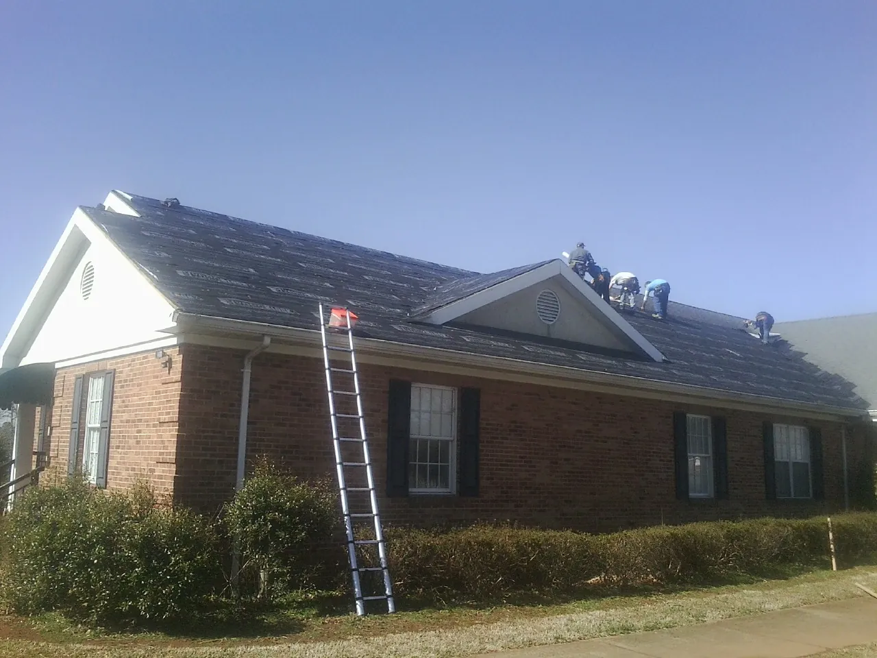 Crew tearing shingles off a brick ranch roof with a ladder set — Emergency Roof Repair work by our crew in Hillrose
