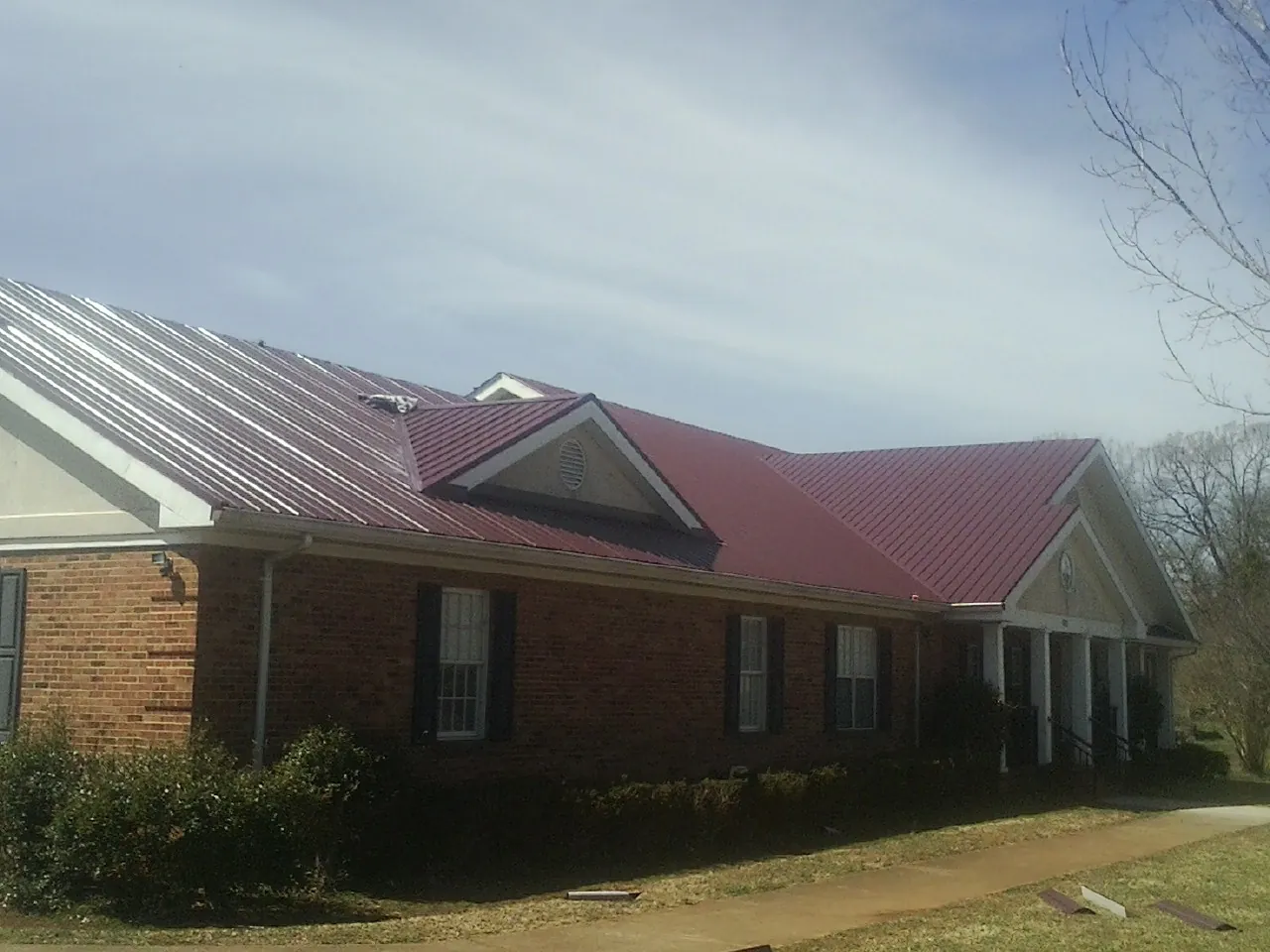 Red metal roof with gabled entries on a long brick building, from a Hail Damage Roof Repair job in Hillrose