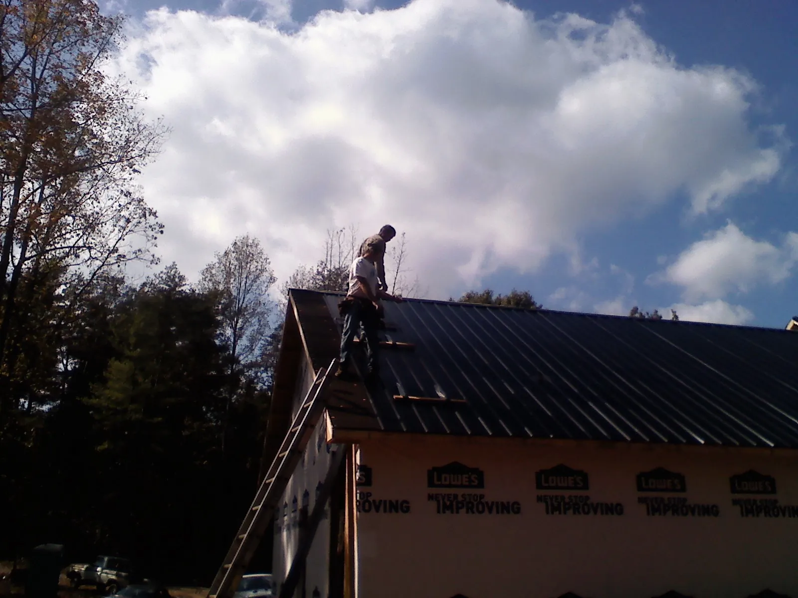 Roofer fastening dark metal panels high against a cloudy sky, from a Roof Inspection job in Hillrose
